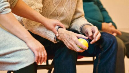 Caregiver al fianco di un anziano con una pallina di plastica tra le mani