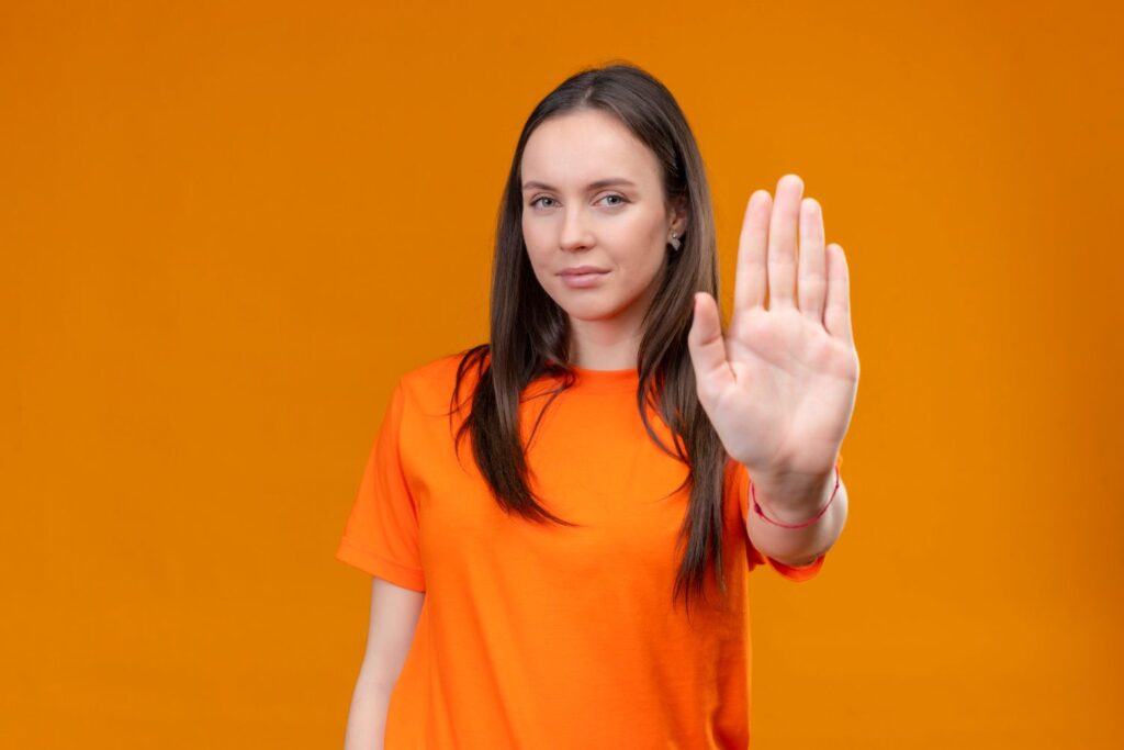 Donna con maglia arancione davanti a sfondo arancione che fa segno stop con la mano