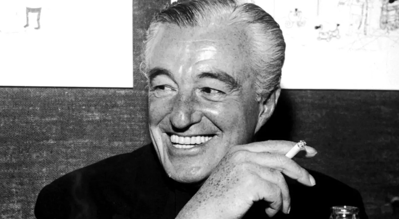 Un'immagine in bianco e nero di Vittorio De Sica mentre sorride con una sigaretta tra le mani