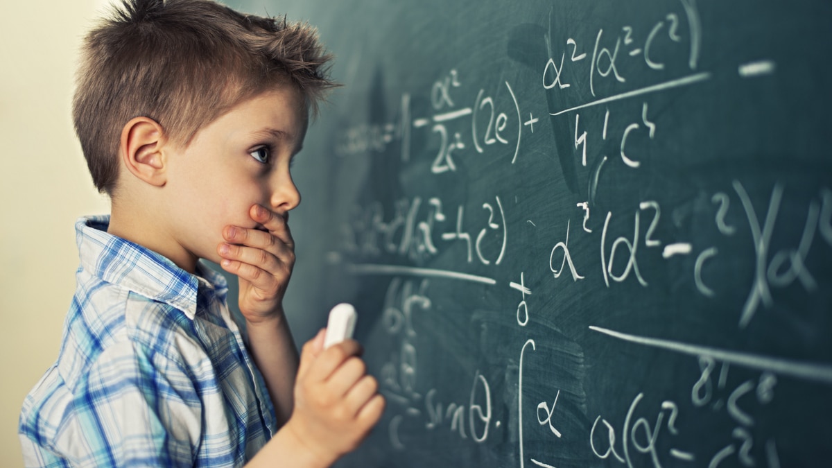 Un bambino con una camicia a quadri celeste che prova a risolvere un problema di matematica alla lavagna